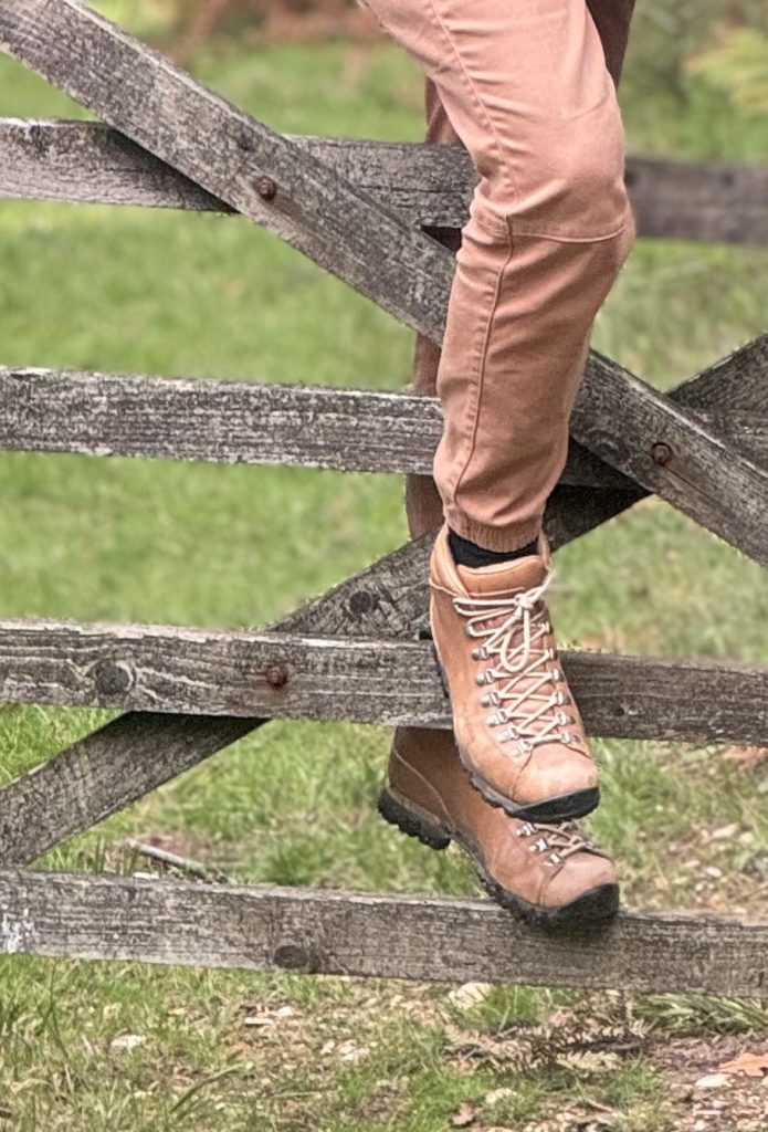 Legs in walking boots climbing over a wooden field gate
